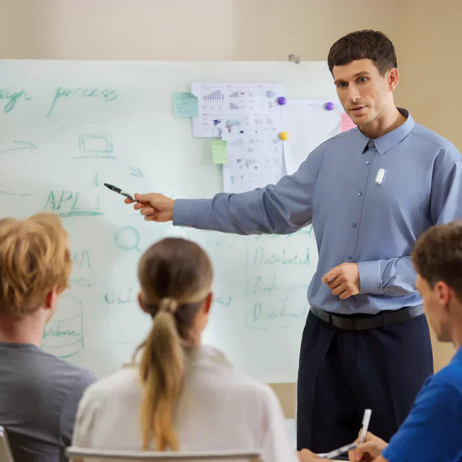 Man presenting with a white Plaud NotePin clipped to his blue shirt, addressing three people in a meeting.