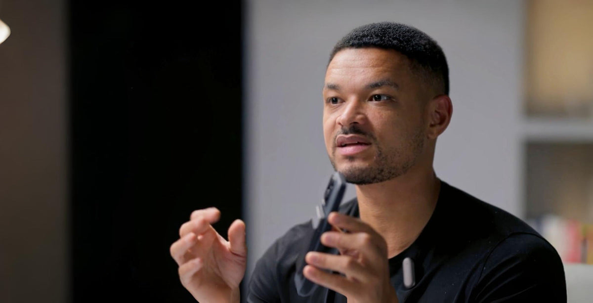 Man speaking and gesturing, wearing a white Plaud NotePin clipped to his black shirt.
