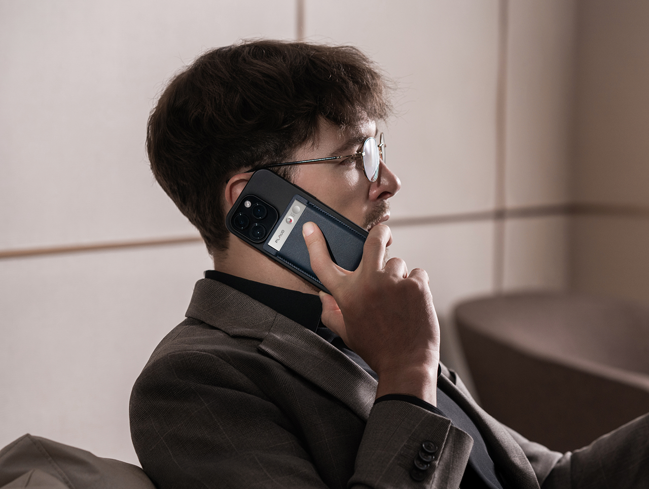 Man in glasses on a phone call, with a black Plaud Note attached to the back of his smartphone.
