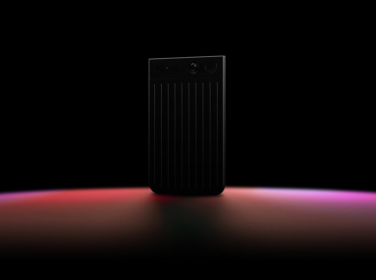 Black Plaud Note Pro standing upright on a dark surface with red and purple light reflections.