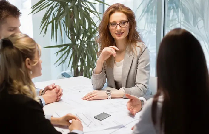 Four professionals in a meeting, with a black Plaud Note on the table amidst blueprints.
