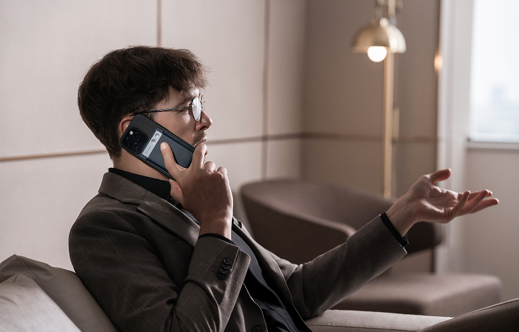Man on a phone call, gesturing, with a black Plaud Note attached to his smartphone.