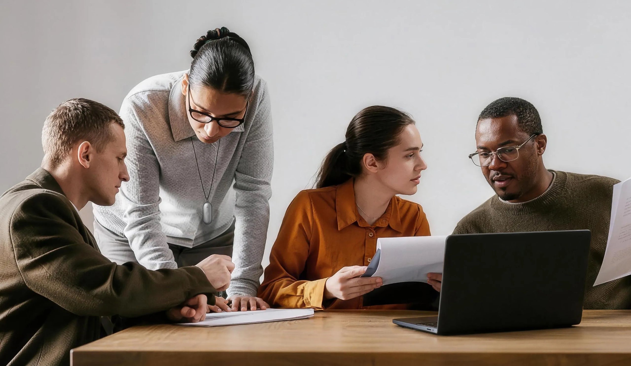 Four diverse professionals collaborating at a table, with a white Plaud NotePin S visible on a lanyard.