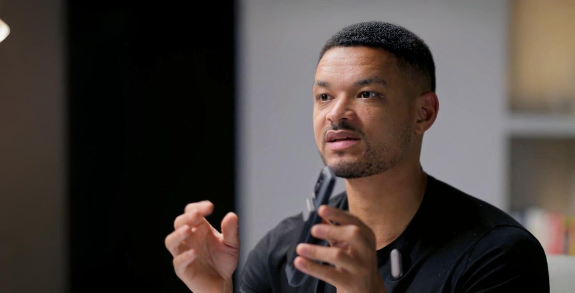 Man speaking and gesturing, wearing a white Plaud NotePin clipped to his black shirt.