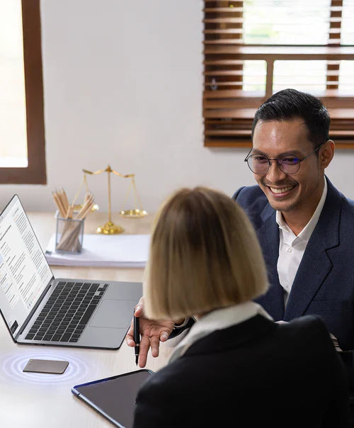 Two professionals in an office, a Plaud Note recording their discussion on a desk with a laptop and tablet.
