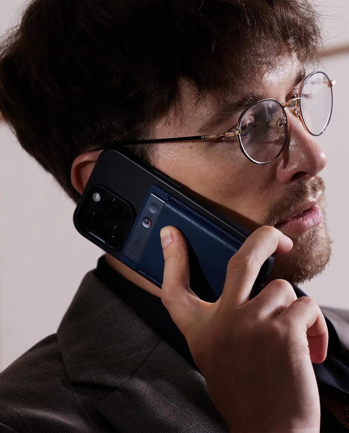 Man on a call, holding a smartphone with a blue Plaud Note attached to the back.