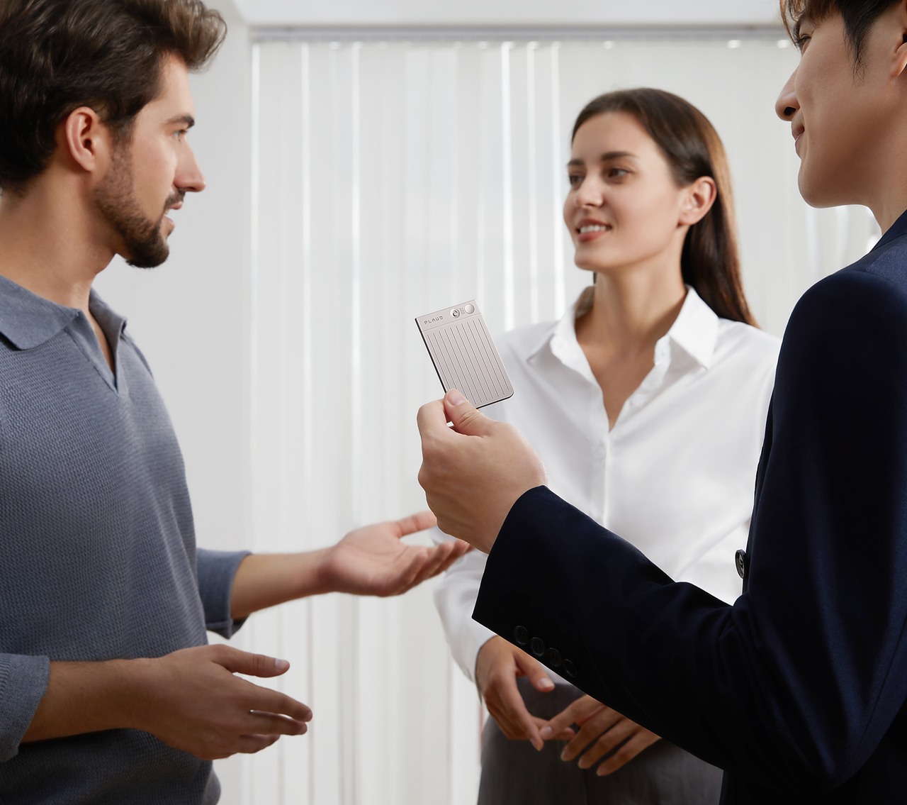 Three professionals in conversation, one presenting a silver Plaud Note Pro AI voice recorder.