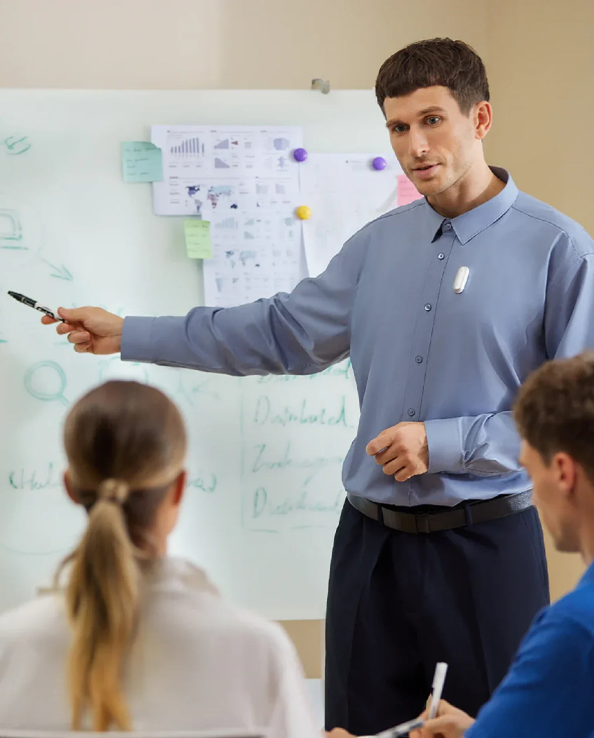 A man presenting in a meeting, wearing a white Plaud NotePin on his shirt, pointing to a whiteboard.