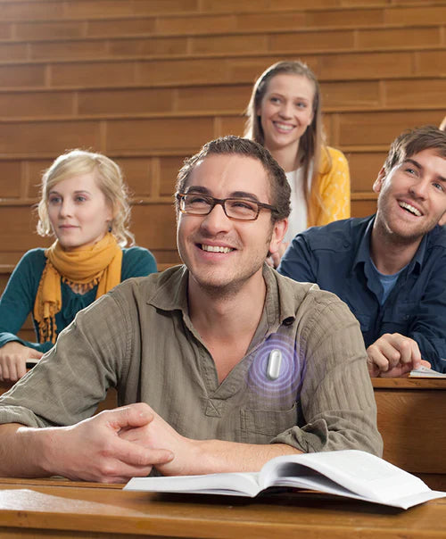 Smiling student in a lecture hall with a white Plaud NotePin AI voice recorder on his shirt.
