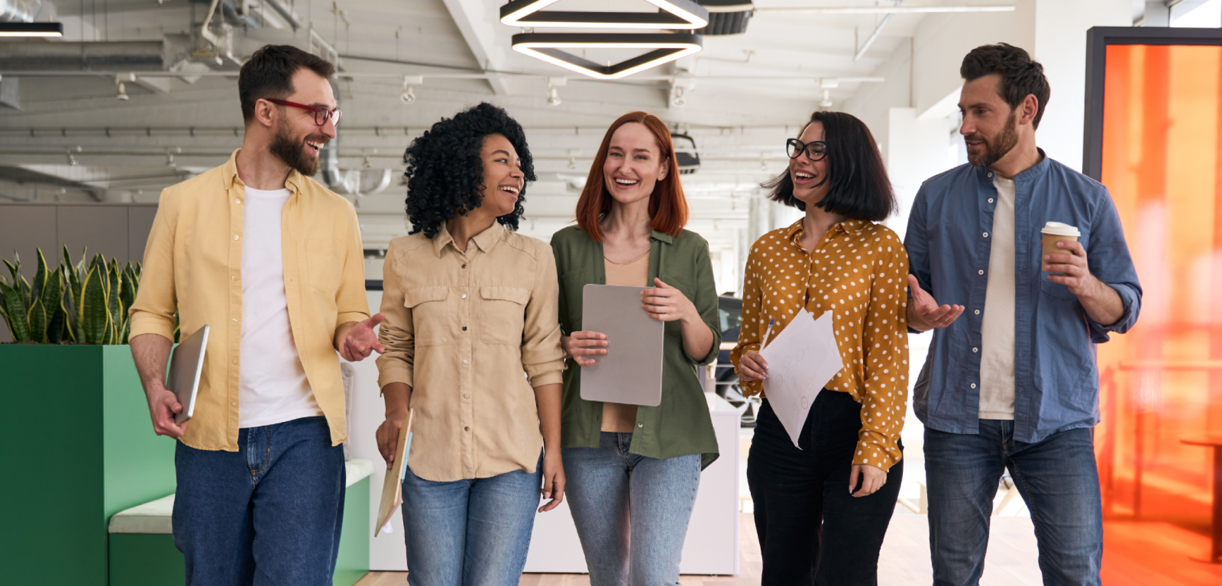 Happy diverse team of five professionals walking and conversing in a modern office.