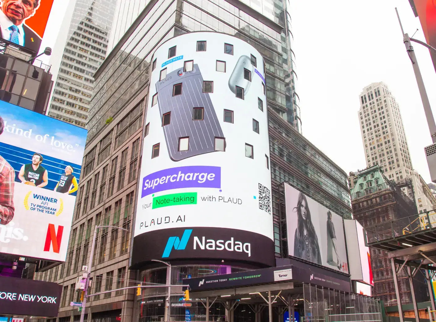 Grey Plaud Note and silver Plaud NotePin on a large digital billboard in Times Square, advertising "Supercharge your Note-tak